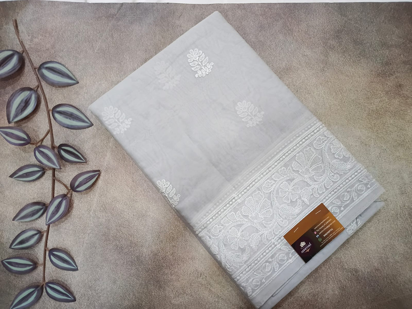 White towel with floral patterns on a beige surface with a branch and leaves.