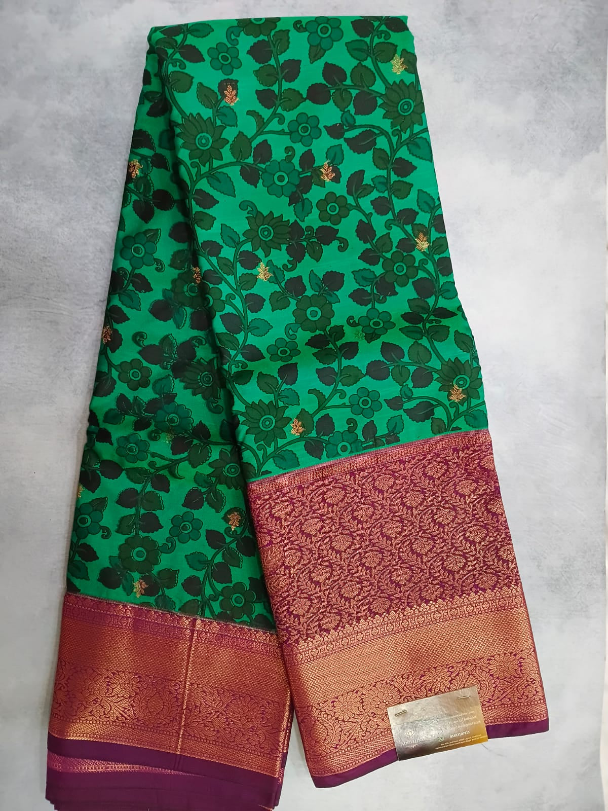 Green floral patterned saree with a pink border on a light gray background