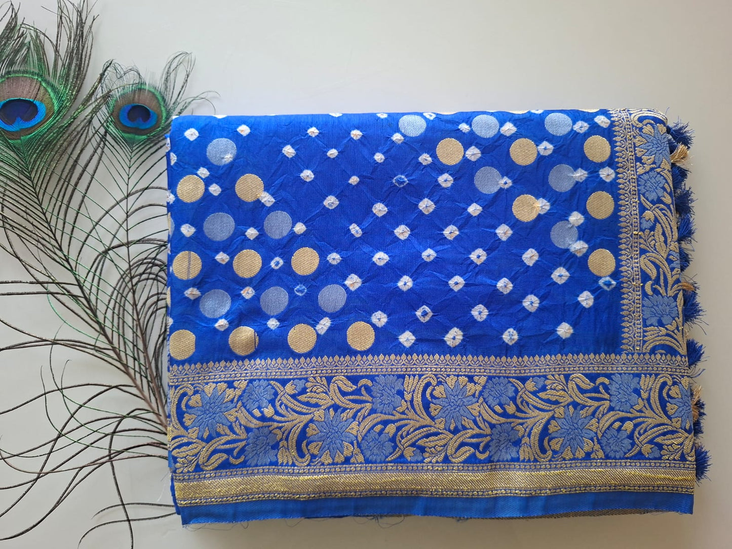 Blue fabric with gold patterns and peacock feathers on a white background