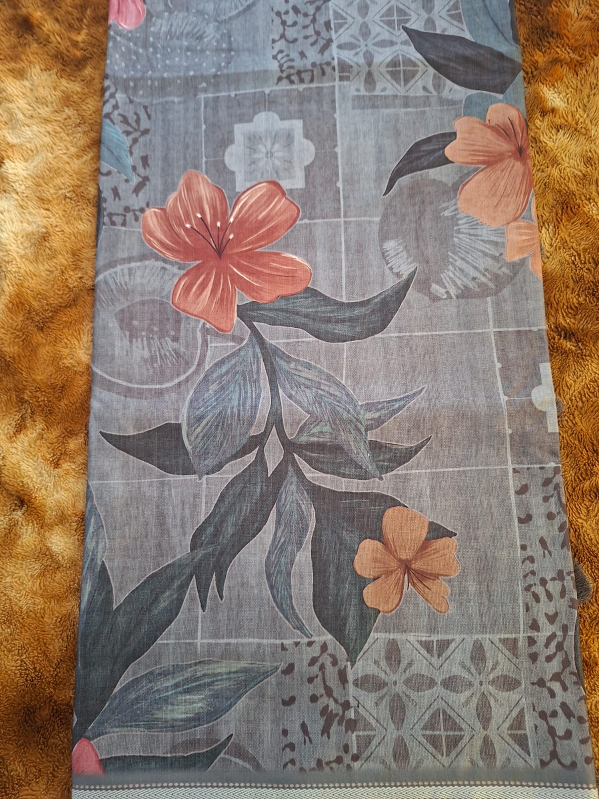 Floral patterned fabric with pink flowers and dark green leaves on a textured brown background