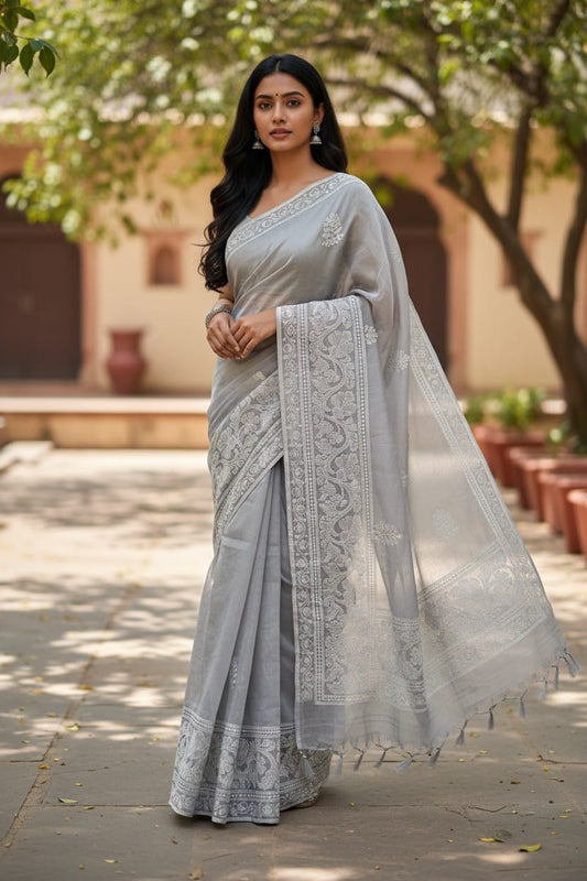 Woman wearing a light gray saree with intricate patterns in an outdoor setting.