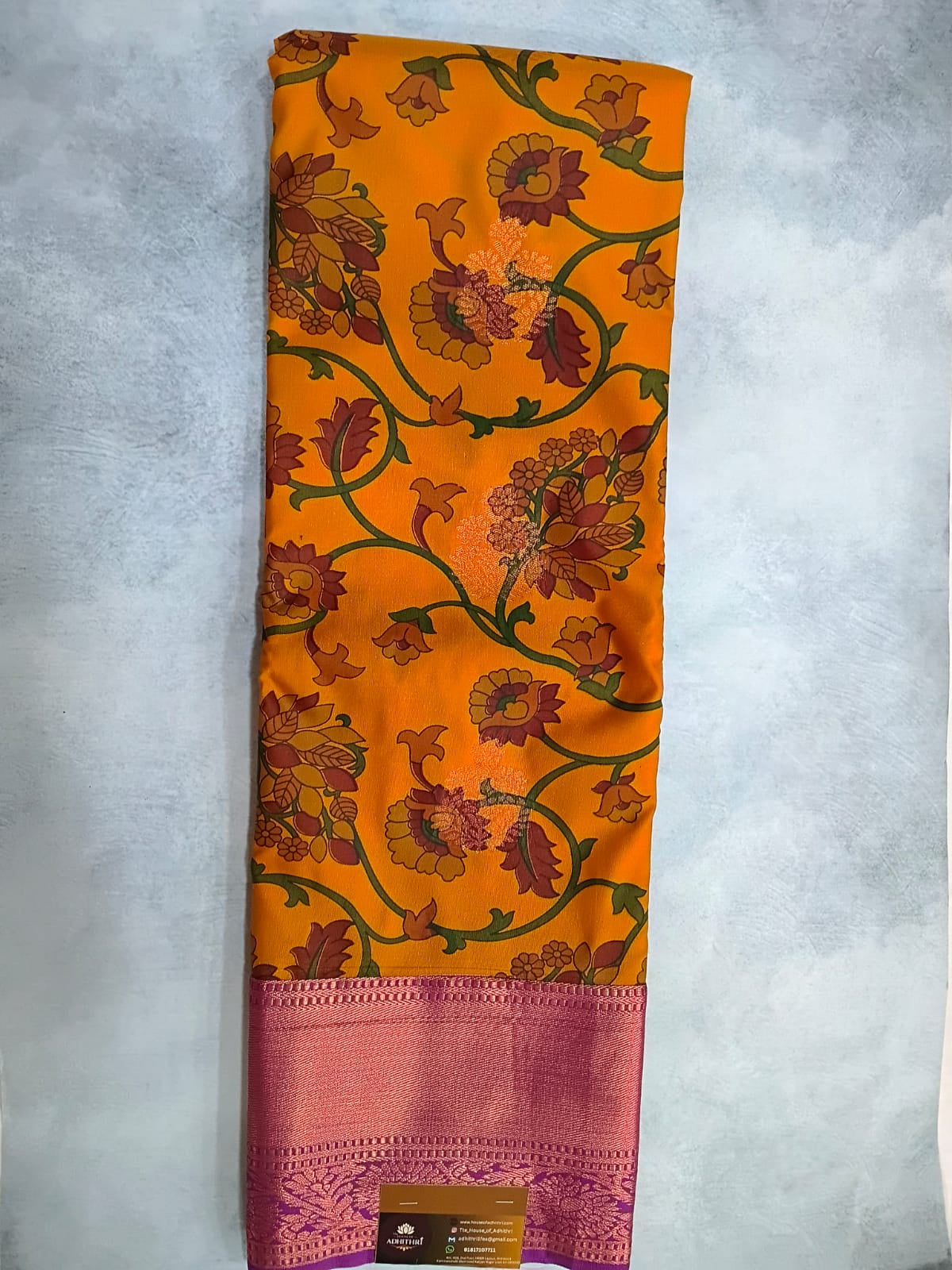 Orange saree with floral patterns and a pink border on a gray background