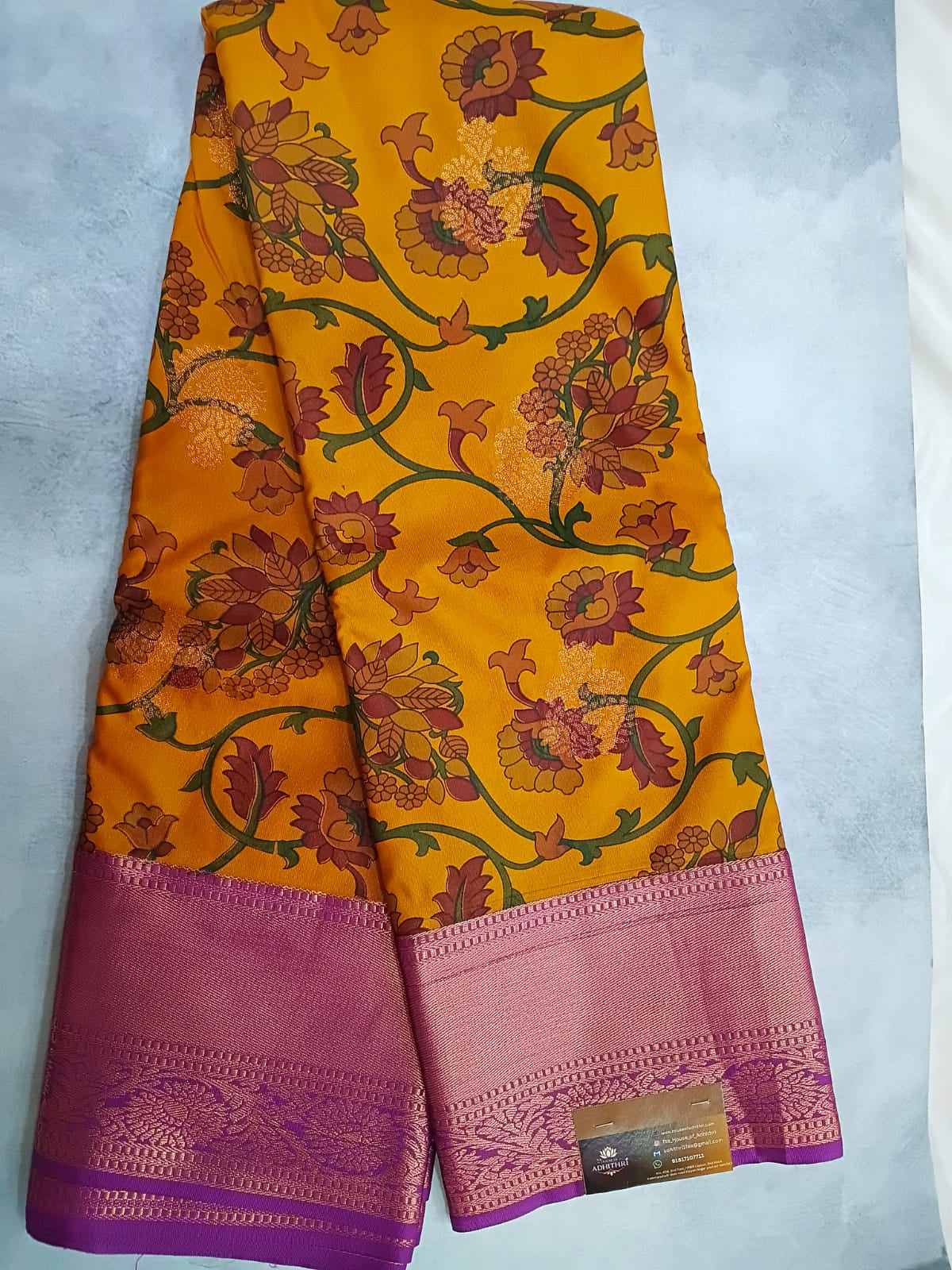 Yellow saree with floral patterns and purple border on a light gray background