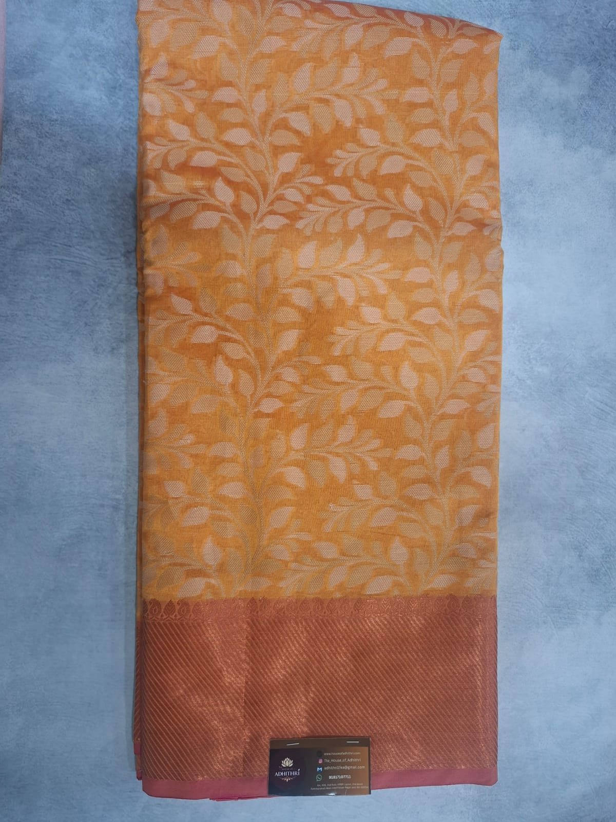 Folded fabric with orange and pink gradient and leaf pattern on a gray background