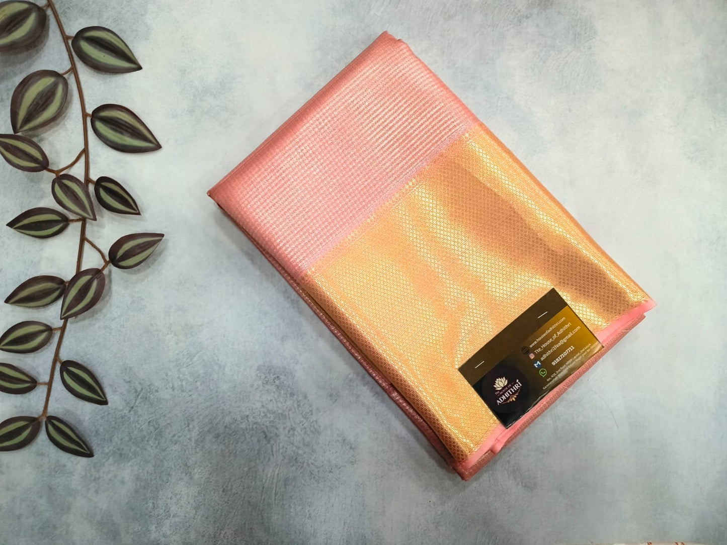 Folded pink and orange fabric on a gray surface with a plant leaf decoration.