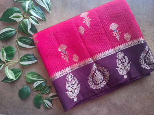Purple and pink sarees with floral patterns on a gray surface with green leaves.