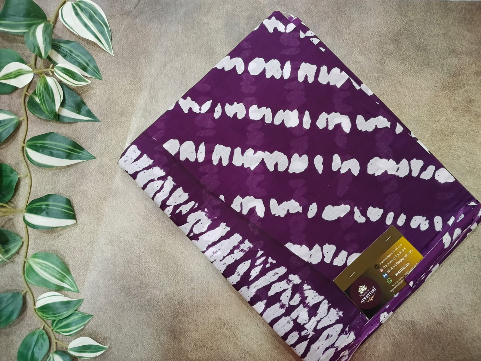 Purple pouch with white pattern on a beige surface with green leaves