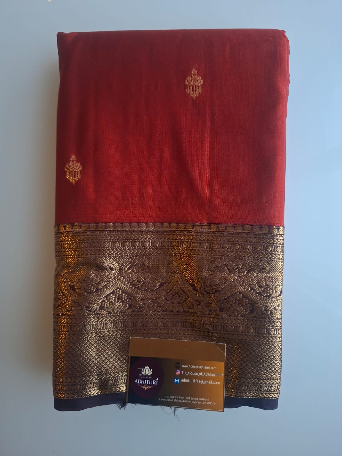 Red fabric with gold embroidery and a visible brand tag on a light blue background