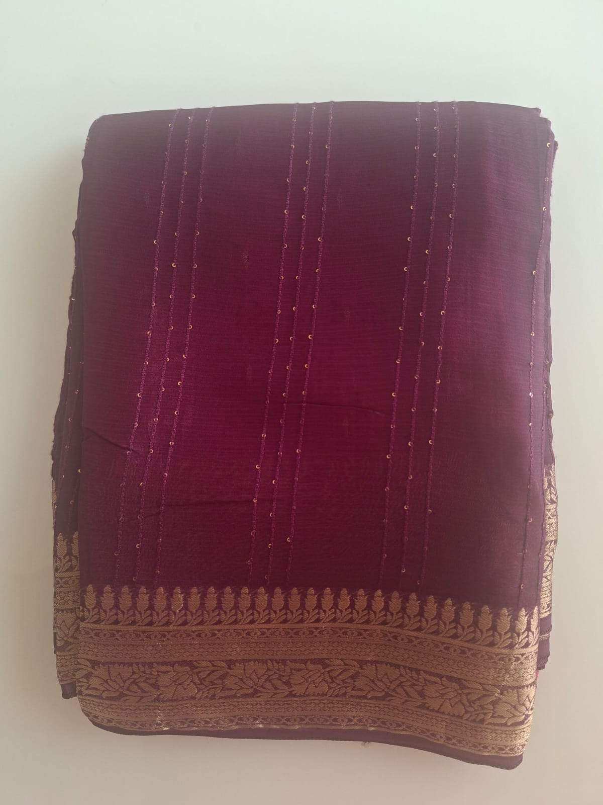 Folded purple fabric with gold embroidery on a white background